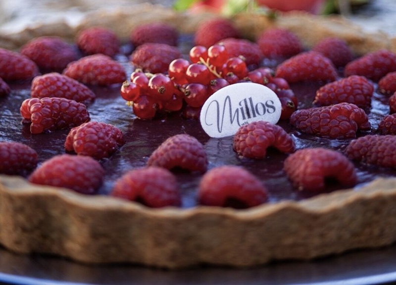 Crostata Millos con lamponi e grappolo di ribes rossi su crema scura lucida, decorata da placchetta bianca col marchio